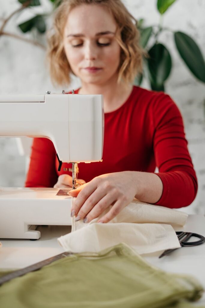 An adult woman in a red dress works on a sewing machine, creating textiles indoors.