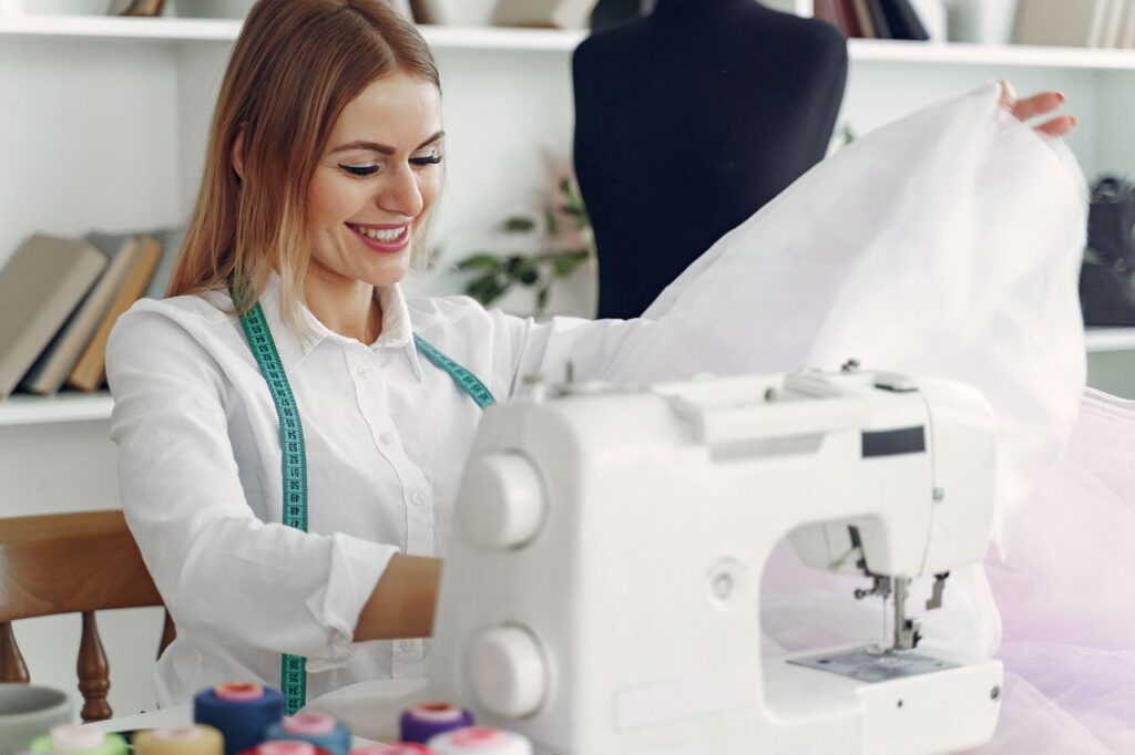 Smiling fashion designer working on a sewing machine with fabric in a contemporary studio.