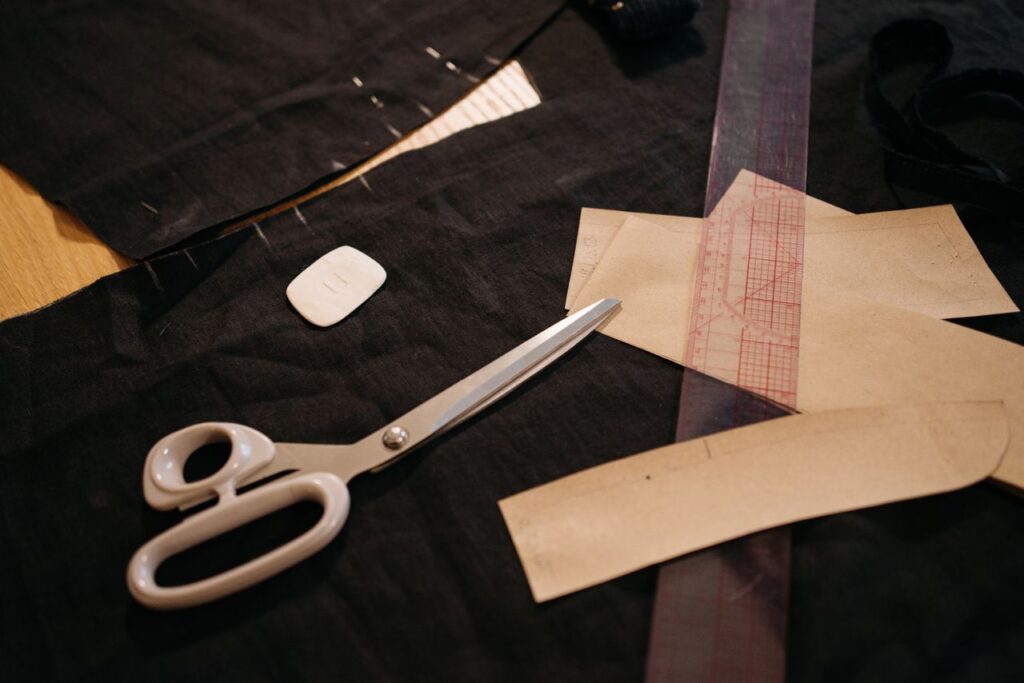 Close-up of tailoring tools including scissors, fabric, and patterns on a workbench.