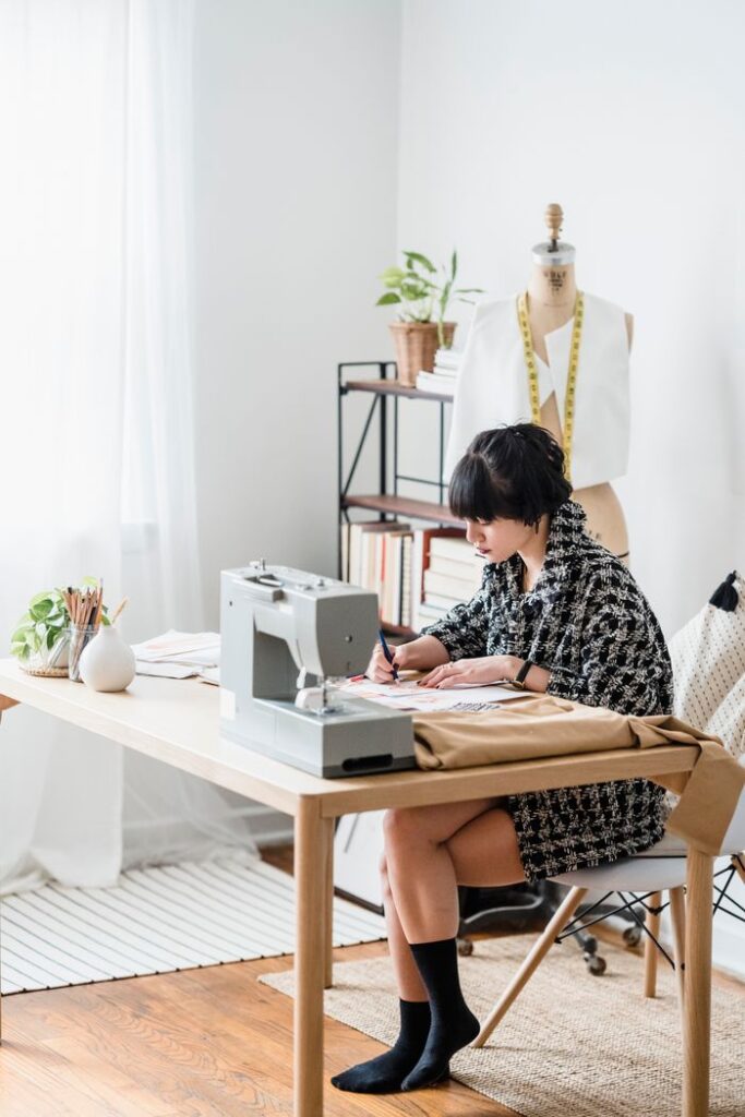 Side view of young concentrated female tailor sitting at table and making sketches while working in modern workshop